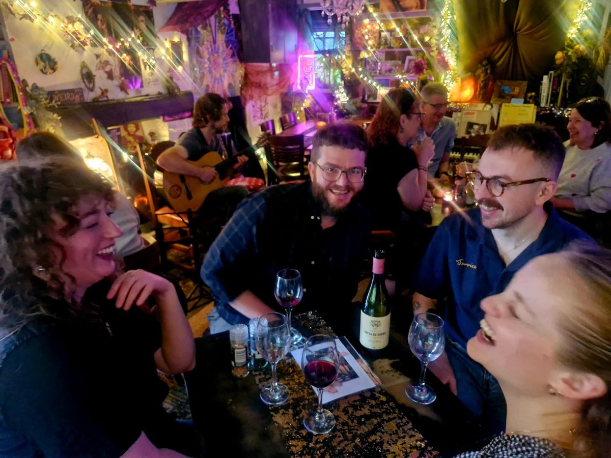 Friends sharing a bottle of red while a guitarist plays behind them