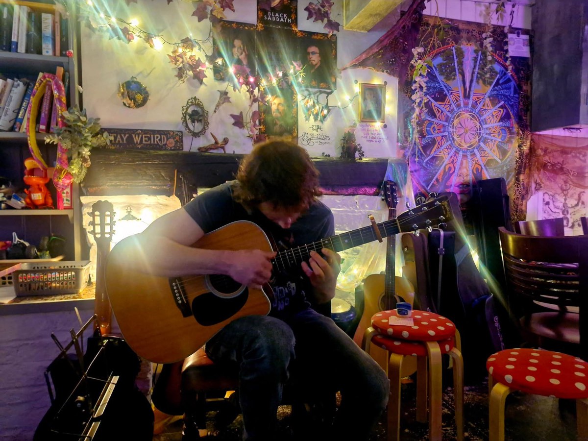 Acoustic guitarist playing under the Stay Weird sign and fairy lights