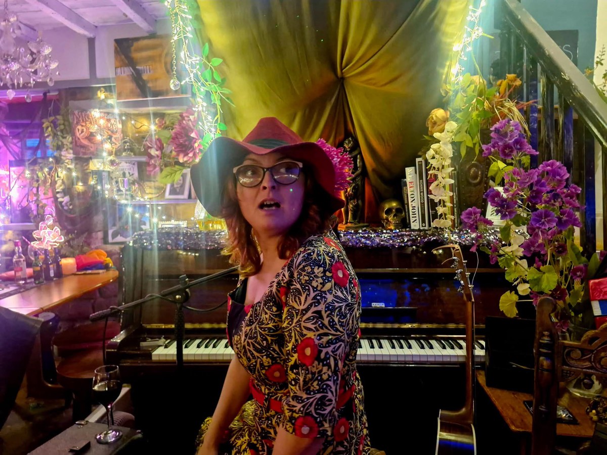A performer in a red hat at the piano under hanging flowers and lights