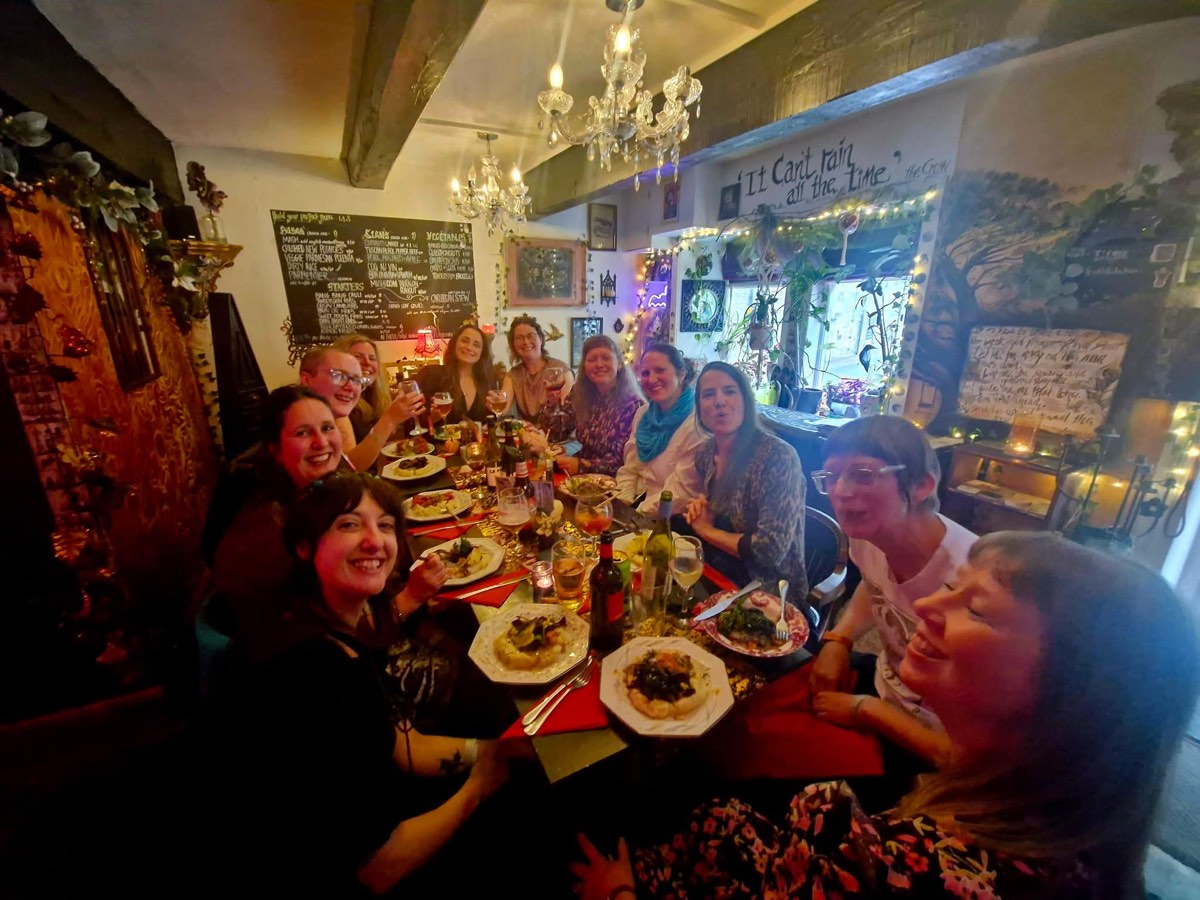 A long-table supper club raising their glasses under the chandeliers
