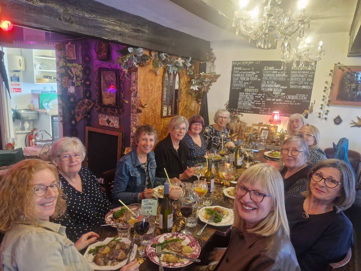 A group lunch around one long table, plates of stew and bottles of wine